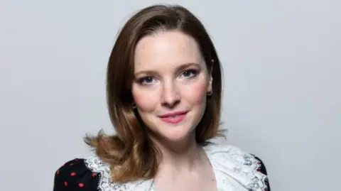 Morfydd Clark, who has brown hair, against a white backdrop