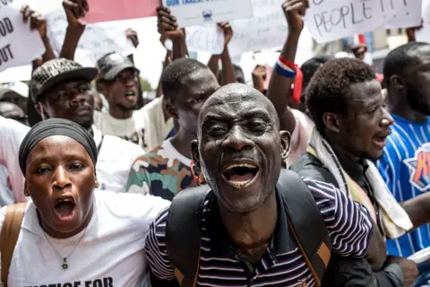 MUHAMADOU BITTAYE / AFP / GETTY IMAGES People chant, shout and wave banners during a march.