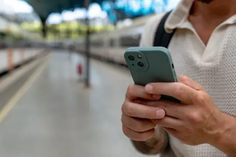 A man holds on a phone on a train station platform