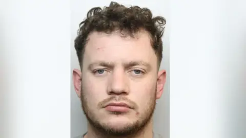 A custody image of Jake Clark, who has short curly brown hair and a short cropped beard.