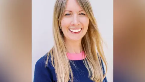 Handout Felicity Winkles, a blonde woman wearing a dark blue jumper with a bright pink collar.