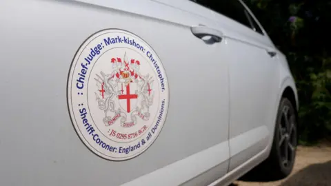 PA Media A white Volkswagen Polo with the crest of Mark Christopher on it. The crest has the St George cross in the middle with dragons either side.