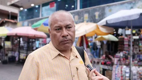 Javier Jaramillo olha para o entrevistador em frente às barracas de alguns vendedores em Caracas