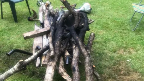 A picture of several pieces of wood that had been set on fire in on the pitch, there is a strimmer and chairs in the background.