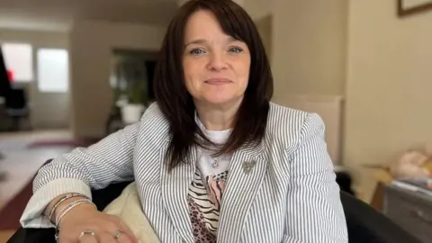 Buffy Williams pictured wearing a striped jacket and a tee-shirt, with a house out of focus in the background.
