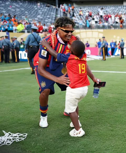 Maja Hitij - FIFA / Getty Images Kenye is seen extending his arms out as his older brother Yamal leans down to pick him up