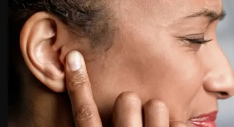 Getty Images A woman shuts her eyes and puts her finger on her ear.
