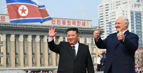 Belarussian Presidency/Anadolu via Getty Images Lukashenko giving a thumbs-up sign, while Kim Jong Un, standing beside him, waves. Behind them is the North Korean flag