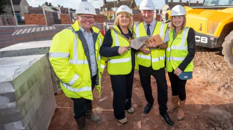 City of Wolverhampton Council Partnership director at Keon Homes, Matt Beckley, Mayor of Wolverhampton, councillor Linda Leach, deputy leader Steve Evans and chief executive at Black Country Housing Group, Amanda Tomlinson are all on the building site in fluorescent jackets and hard hats with the mayor and councillor holding a brick and trowel