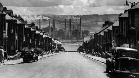 Mirrorpix/Getty Images Dunston Power Station's six chimneys rise into the air with rolling fields behind them The black and white picture was taken amid the dramatic terraces of Clara Street in Newcastle's West End with terraced houses on either side.