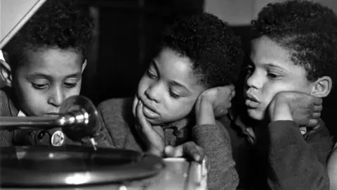 Three young boys from Tiger Bay in 1950 listening to a gramophone.