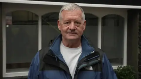 All Post Office Horizon victims entitled to free legal advice for first time 4 Tony Downey Tony Downey, a white man, wearing a black and blue rain coat over a grey t shirt.