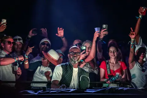 Getty Images South African DJ Black Coffee performs for fans on his DJ decks. Fans are seen in the background dancing.