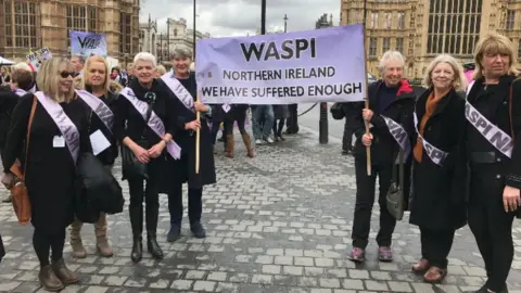 Waspi campaigners outside Westminster. They are holding a sign that says Waspi Northern Ireland We have suffered enough. They wear Waspi sashes and black coats. 