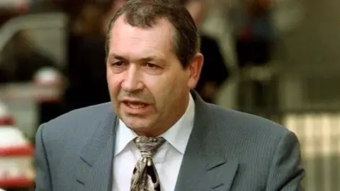 John Palmer is wearing a grey pinstripe suit, white shirt and tie as he walks away from the Old Bailey in 2001
