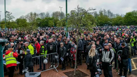 Bike4Life Fest Thousands of people stand in a large crowd. There are grey metal barriers, and people in yellow hi-vis jackets