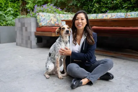 Vivien Wong Vivien Wong sitting cross legged on a patio holding her dog