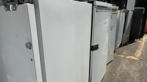A close-up image of about half a dozen appliances next to each other in a line. They are white including the one most prominent in the photo on the left and in the middle of the image.