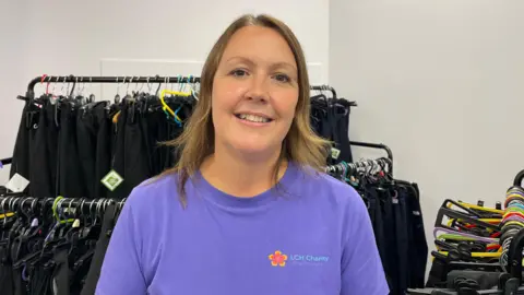 Nichola wearing a purple t-shirt in front of a row of uniform on railings 