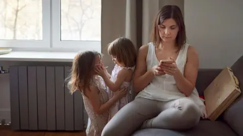 Getty Images Mother with two daughters at home using mobile phone