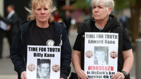     Liam McBurney / PA Campaigners display photos of loved ones who died in the Troubles outside the court
