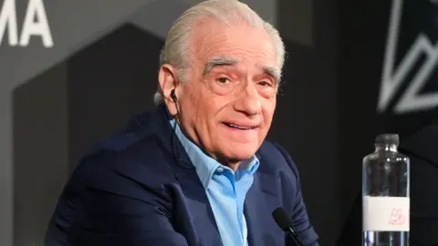 Martin Scorsese in a blue suit with light blue shirt looking at the camera and smiling