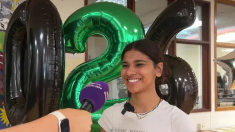 A girl smiles widely in front of balloons