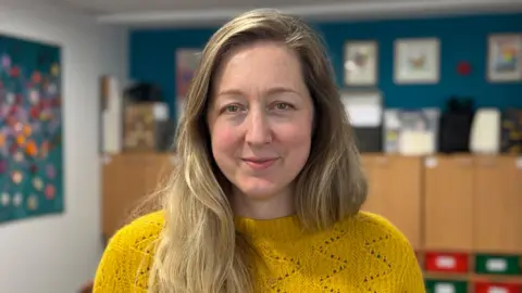 Steph is looking to camera and is wearing a yellow jumper.