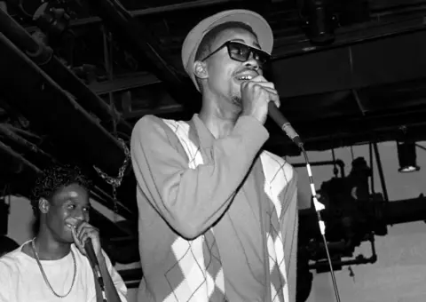 Getty Images A black and white photo depicts Slick Rick on stage at the start of his career in the 1980s