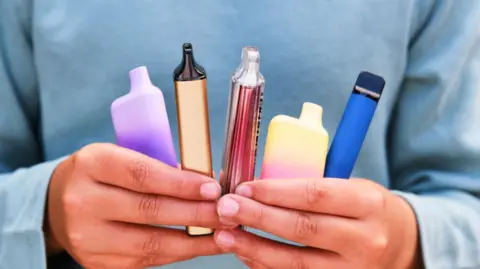 A boy's hands holding five small multi-coloured tube-like containers