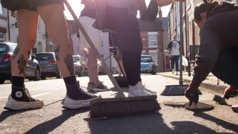 Getty Images Image of residents' feet and brooms as they clean up a Middlesborough street affected by the riots in the UK