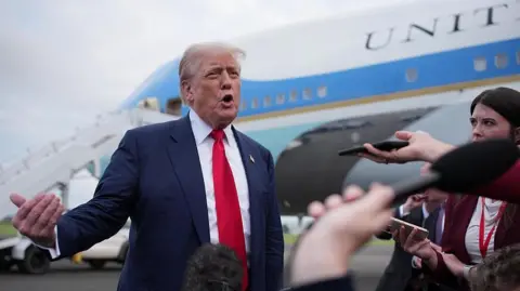 Donald Trump stands speaking to journalists in front of Air Force One