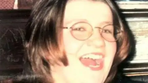 Omagh bombing inquiry Julia Hughes laughs. She has round glasses on with brown eyes and short brown hair.