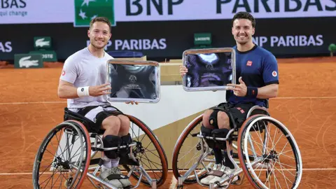 Alfie Hewett and Gordon Reid hold up their French Open men's wheelchair doubles trophies in 2025