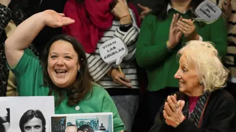 Adriana Metz (left) and Estela de Carlotto, president of the human rights organization Grandmothers of Plaza de Mayo, wave and clap during a news  conference announcing that Metz's brother has been found.