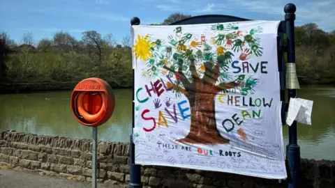 A poster which reads 'save Chellow Dene' erected near a reservoir.