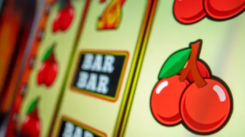 A close-up of a fruit machine, showing cherries and bars