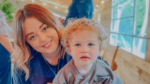 Meg pattern, a curly blonde woman and her little boy smiling on camera, her little boy with short blond curly hair