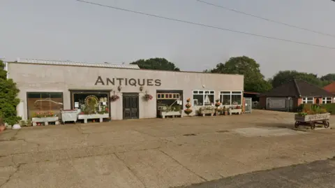 The exterior of the Suffolk Heritage and Antiques Centre in Old London Road in Copdock close to Ipswich. Plants have been set up outside the building and there is a large empty car park.