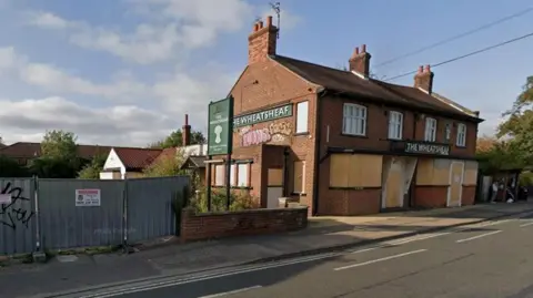 A Google Street View image shows the derelict Wheatsheaf pub. The doors and windows are covered with boards and there is graffiti on the side of the building