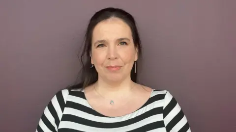 BBC Laura Murtagh - a woman with shoulder length dark hair and wearing a black and white striped top - looks directly into the camera.