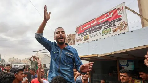 Getty Images Palestinian man on another person's shoulders celebrates in a busy market in Khan Yunis 