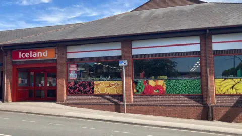 A shopfront with pictures of fruit in the window and an orange and red signage which reads "Iceland"