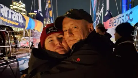 Supplied A father and daughter hug. Behind they are boats. It is dark. 