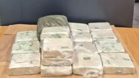 Blocks of heroin, wrapped in clingfilm, placed on top of a wooden table. 