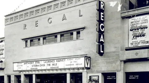 Submitted An old black and white photograph of a cinema with signs that read "Regal" and a board showing the names of films and their cast members