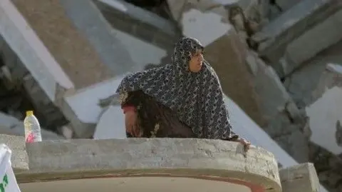 A woman sits in the middle of the rubble and surveys the destruction in Gaza City