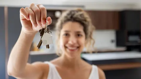 Getty Images Happy woman holding keys while looking at the camera smiling