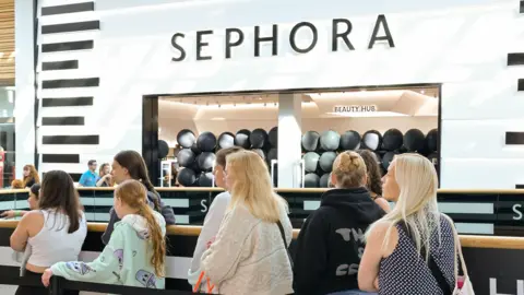 Women queue outside a shop with black and white frontage. Above is a sign that reads: Sephora