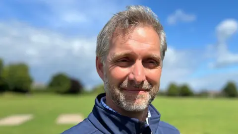 Michael Fowley is wearing a white and blue shirt and a blue jumper